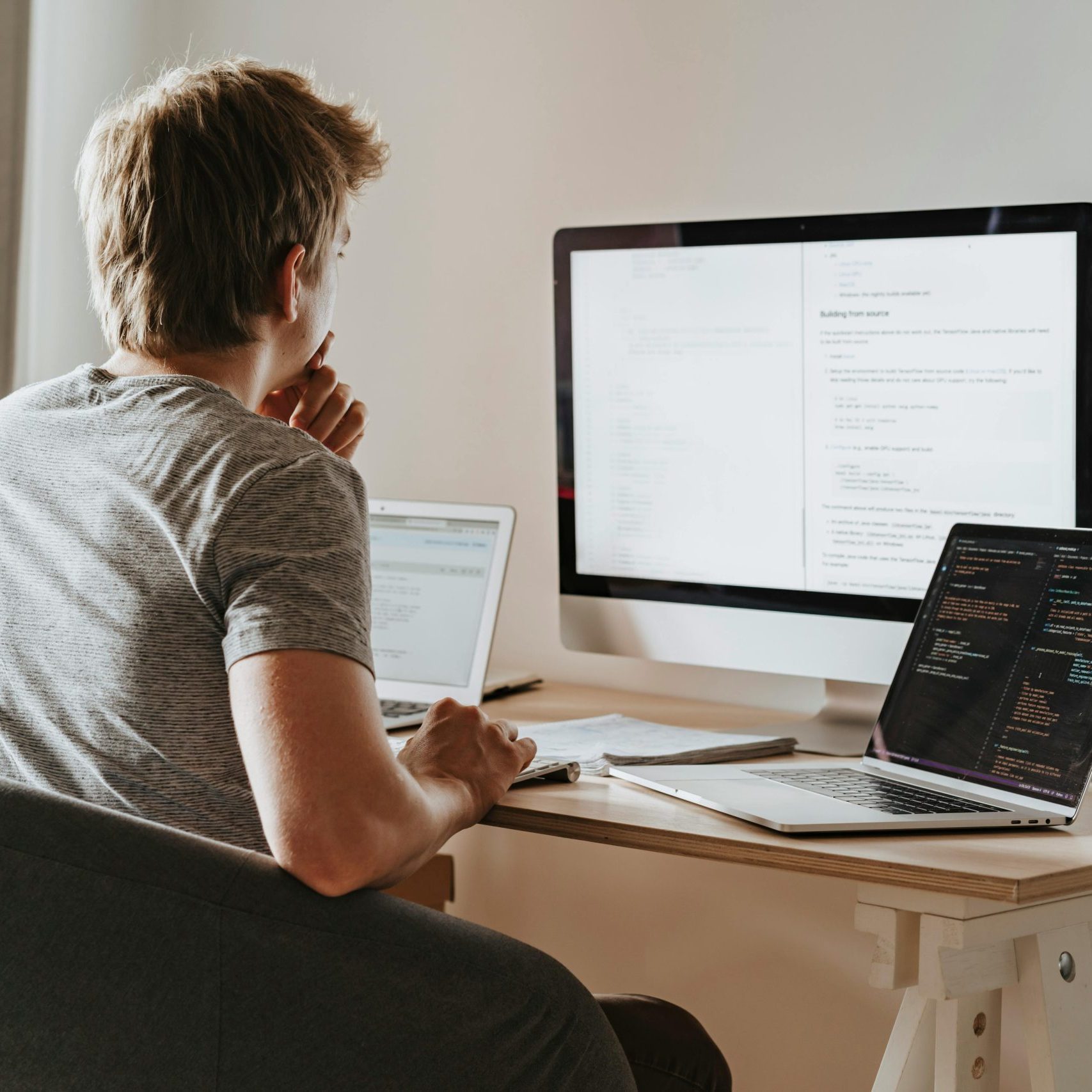 A man deeply engaged in software development with two laptops and a desktop monitor.